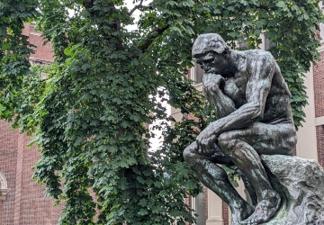The statue Thinker in front of a green tree in summer