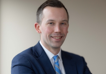 Man with short hair in dark jacket and blue tie