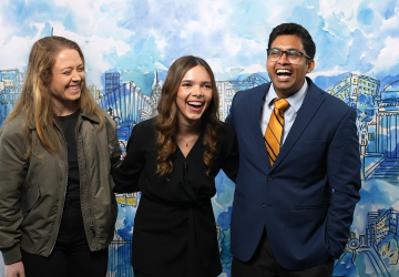 Two women and a man in front of a painted mural