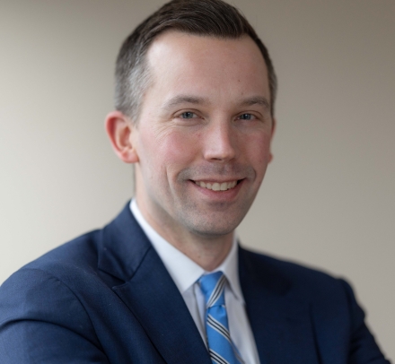 Man with short hair in dark jacket and blue tie