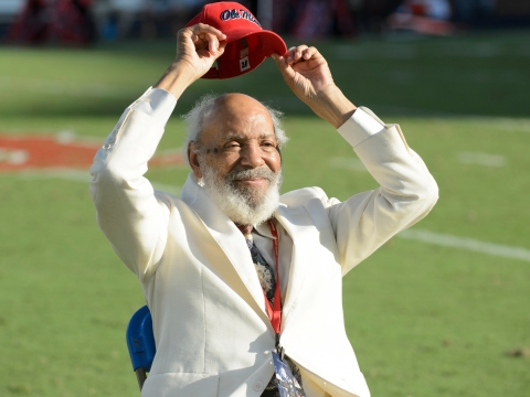A man in a white suit lifts a red "Ole Miss" baseball cap above his head.