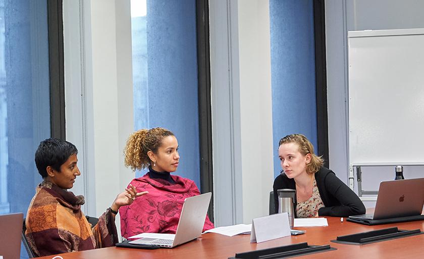Three students with laptops talk in a conference room.