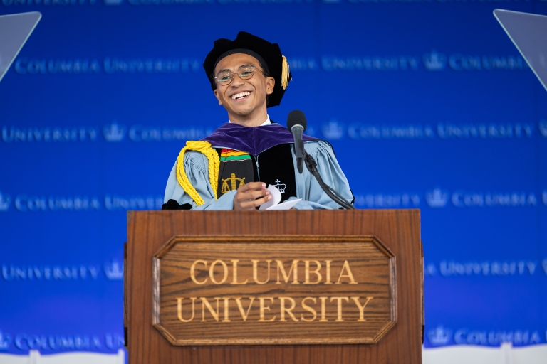 Amir Jones in graduation regalia standing behind a podium
