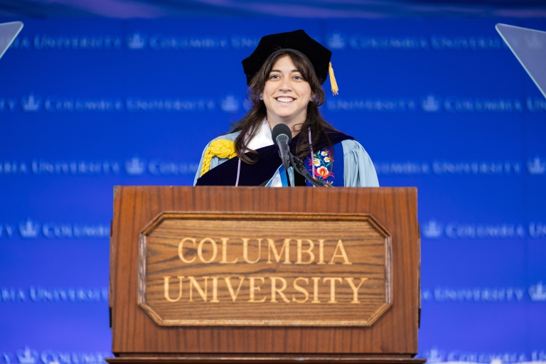 Nicole Morote in graduation regalia behind a podium