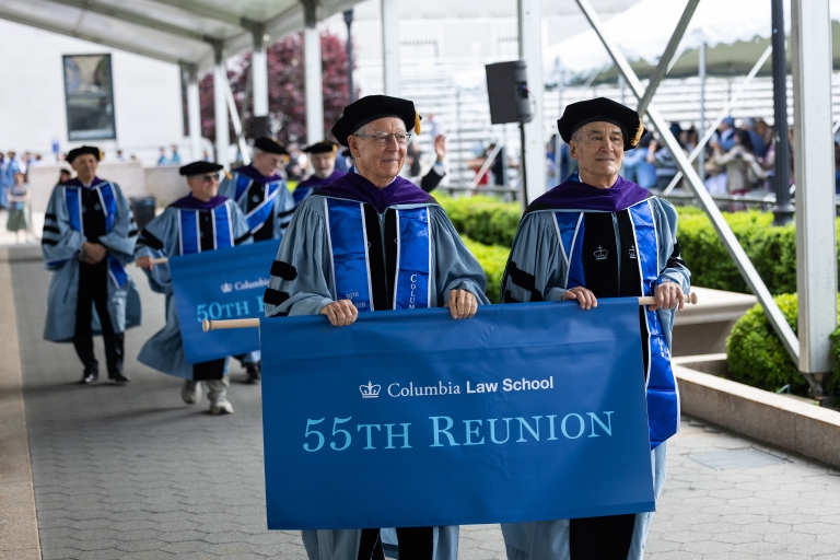 Alumni marching in graduation processional with banner