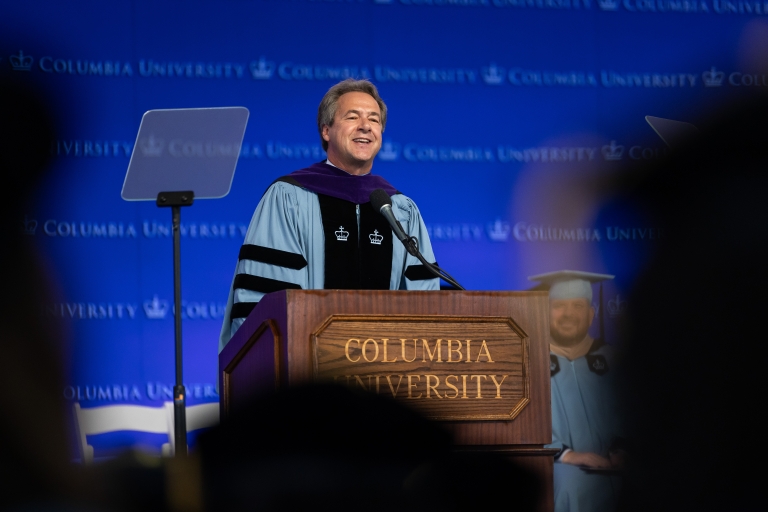 Steve Bullock in academic regalia speaks from the podium at graduation