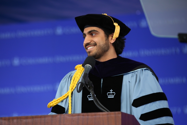 Vedant Chauhan in graduation regalia behind podium