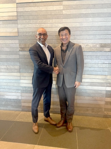 Two men in suits standing and shaking hands in front of a wood-paneled wall