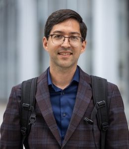 Alexander Hyun in dark shirt and plaid jacket with backpack straps over his shoulders