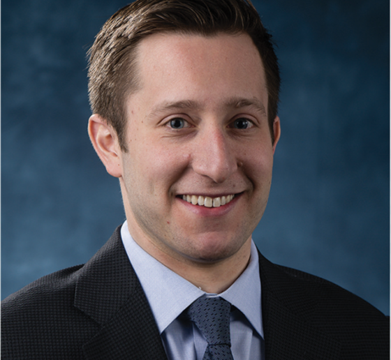 Head shot of man in dark jacket and blue tie. 