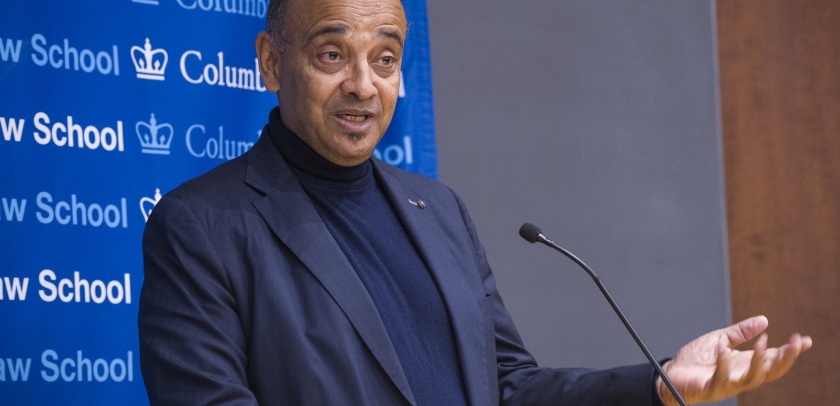 Man speaking at microphone gestures.