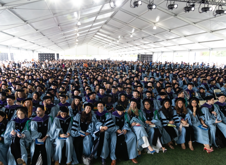 Students in academic regalia seated under enormous tent